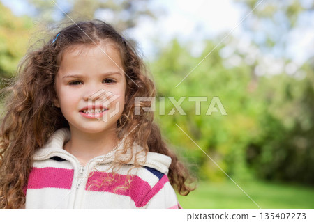 Female child standing in lush garden wearing striped zip-up sweater with hair clips, copy space Female child standing in lush garden wearing striped zip-up sweater with hair clips, copy space 135407273