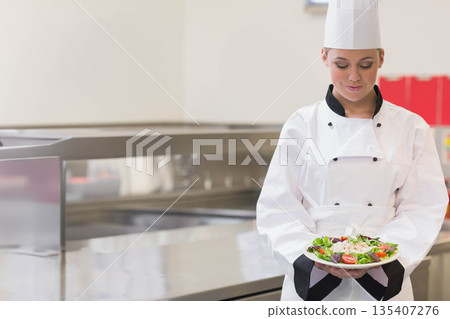 Female chef holding fresh salad plate at steel counter in commercial kitchen, copy space Female chef holding fresh salad plate at steel counter in commercial kitchen, copy space 135407276