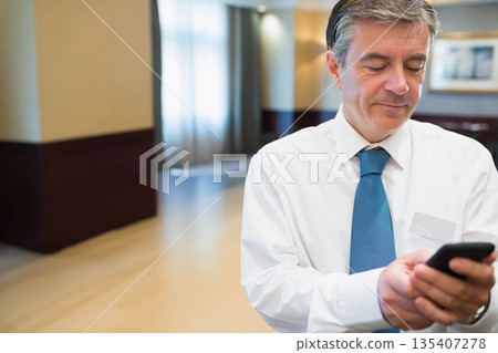 Man standing at conference lobby wearing suit checking smartphone and badge holder, copy space 135407278