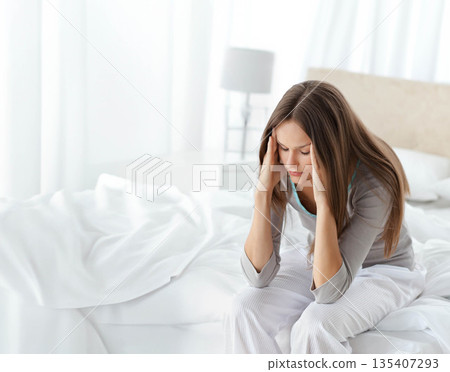 Woman in late 20s sitting on bed pressing temples in bedroom near modern lamp, copy space Woman in late 20s sitting on bed pressing temples in bedroom near modern lamp, copy space 135407293