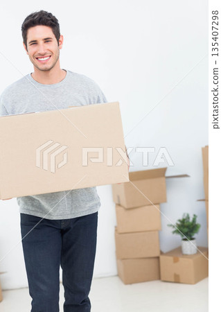 Man holding sealed cardboard box in empty room with moving boxes and potted plant, copy space 135407298