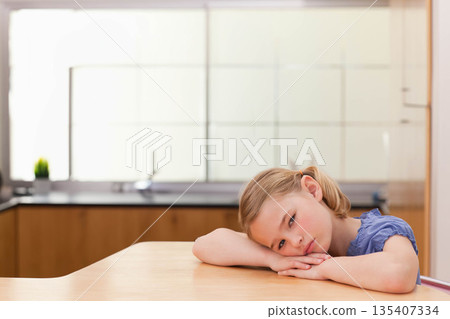 School-age girl leaning on table in kitchen near stainless steel sink and plant, copy space School-age girl leaning on table in kitchen near stainless steel sink and plant, copy space 135407334