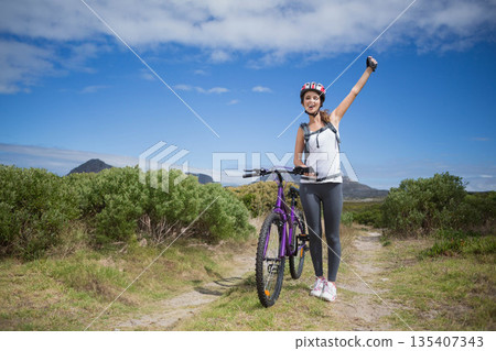 Woman standing beside mountain bike on coastal track checking smartphone wearing helmet, copy space Woman standing beside mountain bike on coastal track checking smartphone wearing helmet, copy space 135407343