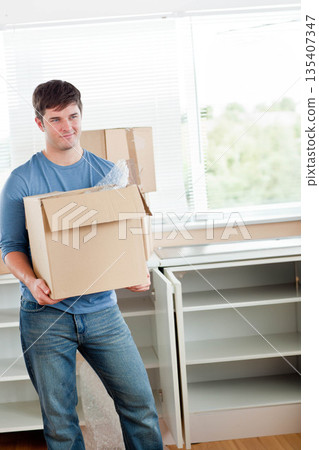 Man in his thirties wearing clothes carrying moving box with packing material at home, copy space Man in his thirties wearing clothes carrying moving box with packing material at home, copy space 135407347
