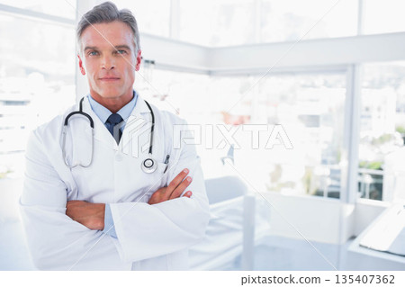 Mature male doctor standing with folded arms in medical clinic with stethoscope, lab coat Mature male doctor standing with folded arms in medical clinic with stethoscope, lab coat 135407362