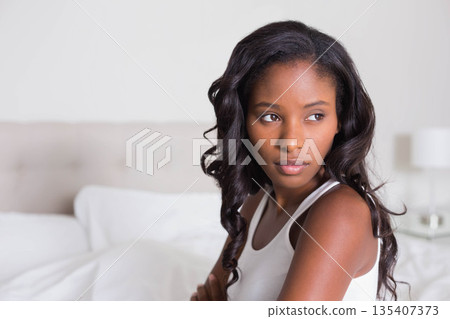 African American woman sitting on bed in bedroom with tufted headboard, table lamp, copy space African American woman sitting on bed in bedroom with tufted headboard, table lamp, copy space 135407373