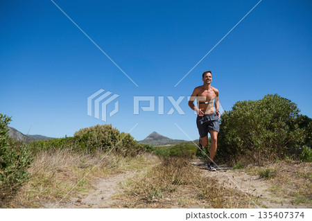 Man running on sandy trail wearing shorts, running shoes, heart-rate strap, wristwatch, copy space Man running on sandy trail wearing shorts, running shoes, heart-rate strap, wristwatch, copy space 135407374