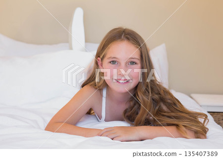 Female child lying in bed in bedroom with white headboard and wicker basket smiling at camera 135407389