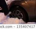 Person Stepping into Snow Near a Stuck Car Wheel 135407417