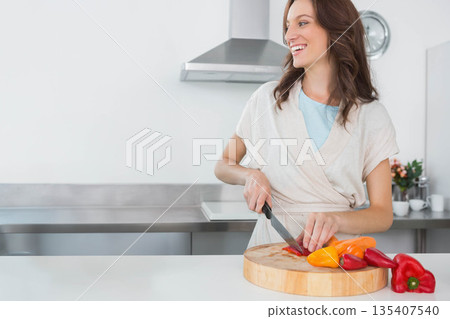 Woman slicing red and yellow bell peppers on wooden cutting board at kitchen counter, copy space Woman slicing red and yellow bell peppers on wooden cutting board at kitchen counter, copy space 135407540