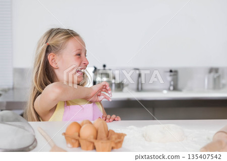 Child girl wearing pink apron behind floured counter mixing egg dough near kettle, copy space 135407542