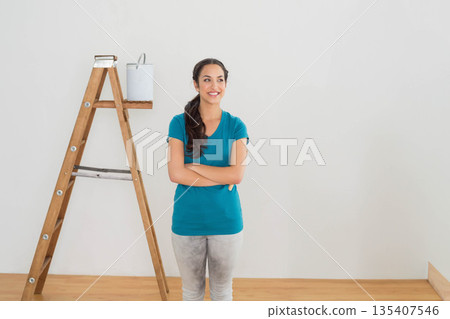 Woman holding bucket of white paint next to wooden stepladder in bright room with hardwood floor Woman holding bucket of white paint next to wooden stepladder in bright room with hardwood floor 135407546