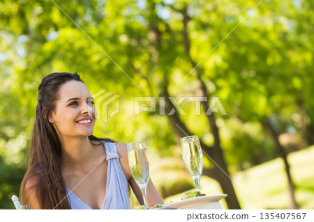 Woman smiling, sitting at park table in blue dress holding champagne flute and appetizer plate Woman smiling, sitting at park table in blue dress holding champagne flute and appetizer plate 135407567
