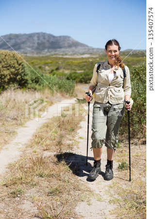 Woman hiking on dry hillside trail wearing jacket with trekking poles and backpack, copy space Woman hiking on dry hillside trail wearing jacket with trekking poles and backpack, copy space 135407574