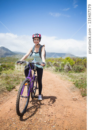 Woman standing on dirt trail holding purple mountain bike wearing cycling helmet and hydration pack Woman standing on dirt trail holding purple mountain bike wearing cycling helmet and hydration pack 135407579
