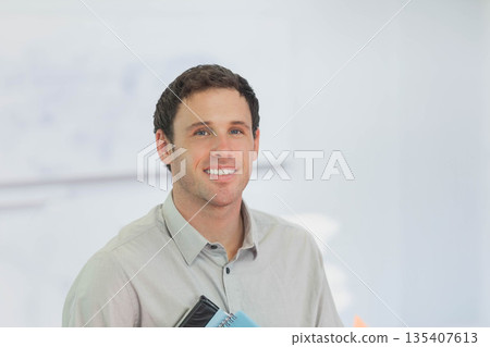 Man in his thirties wearing gray shirt holding notebooks and folders in bright office, copy space Man in his thirties wearing gray shirt holding notebooks and folders in bright office, copy space 135407613