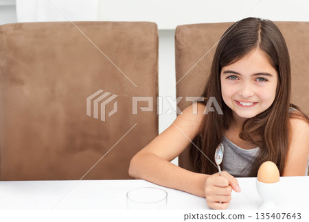 Female child sitting at dining table holding spoon over soft-boiled egg and glass, copy space 135407643
