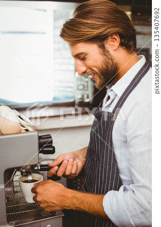 Adult male barista locking portafilter on espresso machine and pulling shot into cup behind counter Adult male barista locking portafilter on espresso machine and pulling shot into cup behind counter 135407692