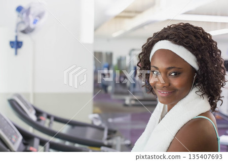 African American woman standing next to treadmill in gym with towel and earphones, copy space African American woman standing next to treadmill in gym with towel and earphones, copy space 135407693