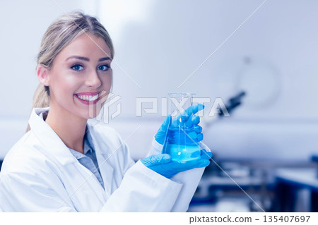 Female scientist holding beaker with blue liquid wearing nitrile gloves at lab bench, copy space Female scientist holding beaker with blue liquid wearing nitrile gloves at lab bench, copy space 135407697