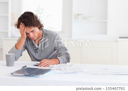 Male sitting at table in bright kitchen working on finances with calculator receipts folder mug Male sitting at table in bright kitchen working on finances with calculator receipts folder mug 135407701
