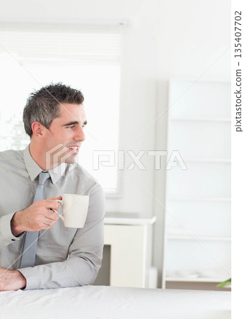 Man wearing gray shirt sitting at table in office holding mug facing left, copy space Man wearing gray shirt sitting at table in office holding mug facing left, copy space 135407702