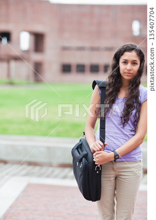 Woman standing on campus walkway holding black messenger bag and checking wristwatch, copy space Woman standing on campus walkway holding black messenger bag and checking wristwatch, copy space 135407704