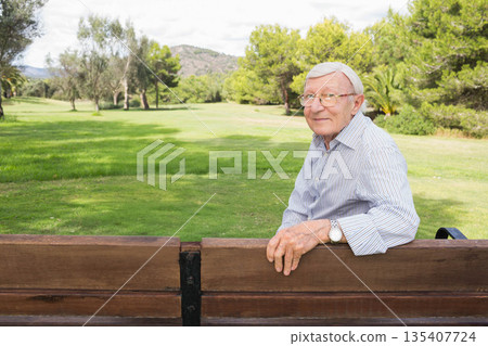 Senior man leaning on wooden bench in park wearing wristwatch and eyeglasses, copy space Senior man leaning on wooden bench in park wearing wristwatch and eyeglasses, copy space 135407724
