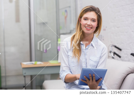 Female wearing blue shirt holding tablet smiling on couch in lounge with sticky notes bike handles Female wearing blue shirt holding tablet smiling on couch in lounge with sticky notes bike handles 135407747