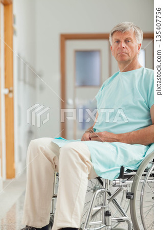 Senior man sitting in wheelchair wearing green medical gown in hospital corridor, copy space Senior man sitting in wheelchair wearing green medical gown in hospital corridor, copy space 135407756