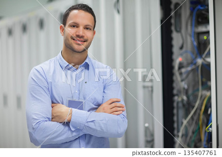 Male IT technician standing with arms crossed in data center server cabinets and cables, copy space 135407761