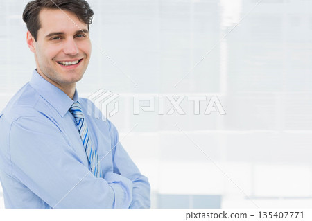 Man standing with arms crossed smiling in office sporting blue shirt and striped tie, copy space Man standing with arms crossed smiling in office sporting blue shirt and striped tie, copy space 135407771