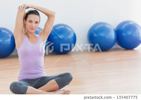 Woman in sportswear doing shoulder stretch in fitness studio with blue stability balls, copy space 135407775