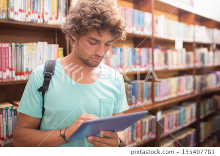 Man standing between wooden bookshelves in library aisle scanning tablet screen wearing backpack Man standing between wooden bookshelves in library aisle scanning tablet screen wearing backpack 135407781