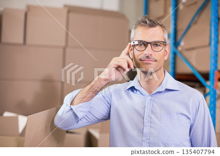 Man in shirt adjusting smart glasses in warehouse by open box and stacked boxes, copy space 135407794
