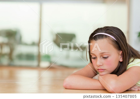 School-age girl resting on arms on wooden floor near glass doors wearing pink headband, copy space School-age girl resting on arms on wooden floor near glass doors wearing pink headband, copy space 135407805