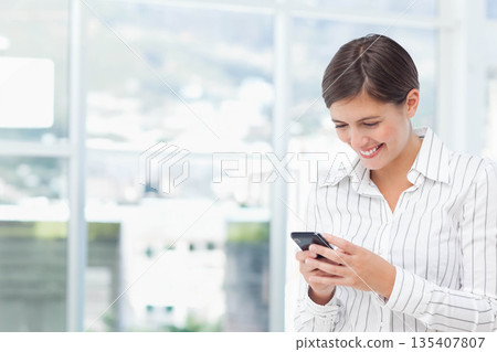 Female office worker wearing striped shirt standing by lobby window checking smartphone copy space Female office worker wearing striped shirt standing by lobby window checking smartphone copy space 135407807