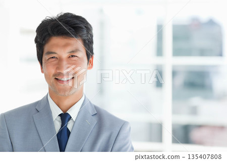 Mid adult Japanese man smiling in business attire in office with blurred cityscape view, copy space Mid adult Japanese man smiling in business attire in office with blurred cityscape view, copy space 135407808