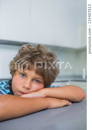Child boy resting head on forearms on gray kitchen countertop under handle-less white cabinets Child boy resting head on forearms on gray kitchen countertop under handle-less white cabinets 135407813