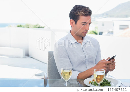 Man checking smartphone at terrace with salad and wine at table overlooking sea, copy space Man checking smartphone at terrace with salad and wine at table overlooking sea, copy space 135407831