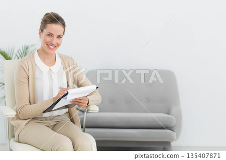 Woman sitting on white swivel chair in consulting room writing notes with pen on clipboard 135407871