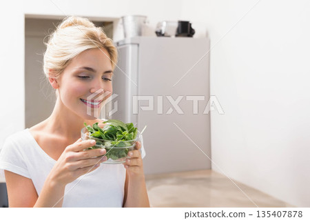 Woman smelling leafy greens in glass bowl in home kitchen near steel refrigerator, copy space Woman smelling leafy greens in glass bowl in home kitchen near steel refrigerator, copy space 135407878