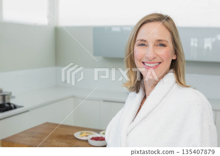 Woman standing smiling in white kitchen at wooden island with raspberries and toast, copy space Woman standing smiling in white kitchen at wooden island with raspberries and toast, copy space 135407879