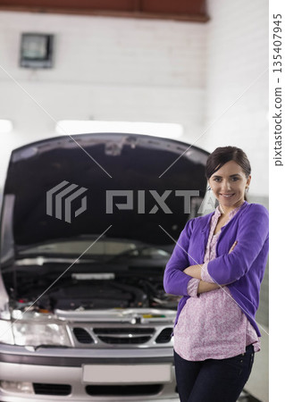 Woman standing beside silver sedan with open hood and visible engine bay in garage, copy space Woman standing beside silver sedan with open hood and visible engine bay in garage, copy space 135407945