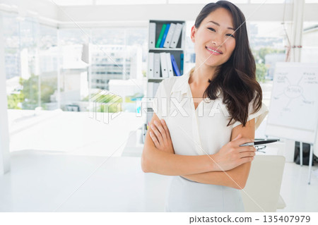 Asian female standing crossing arms and holding eyeglasses beside flipchart in office, copy space 135407979