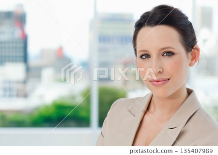 Female executive standing in office wearing blazer viewing skyscrapers through window, copy space Female executive standing in office wearing blazer viewing skyscrapers through window, copy space 135407989