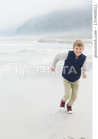 Male child running along sandy shore at beach wearing red sneakers, leaving footprints, copy space Male child running along sandy shore at beach wearing red sneakers, leaving footprints, copy space 135408011