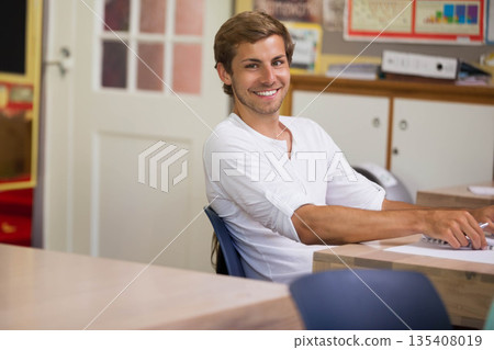 Male student typing on keyboard at classroom desk with papers and bulletin board, copy space Male student typing on keyboard at classroom desk with papers and bulletin board, copy space 135408019