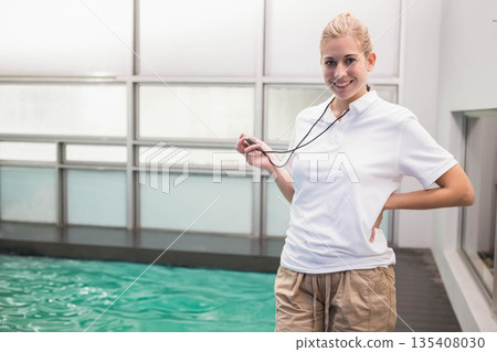 Female swim instructor smiling, holding stopwatch on pool deck beside frosted windows, copy space Female swim instructor smiling, holding stopwatch on pool deck beside frosted windows, copy space 135408030