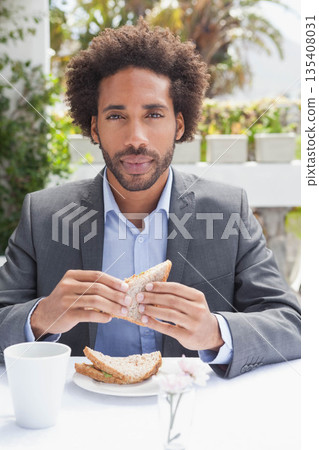 African American man holding whole-grain sandwich at cafe patio wearing blazer with mug and flower 135408031